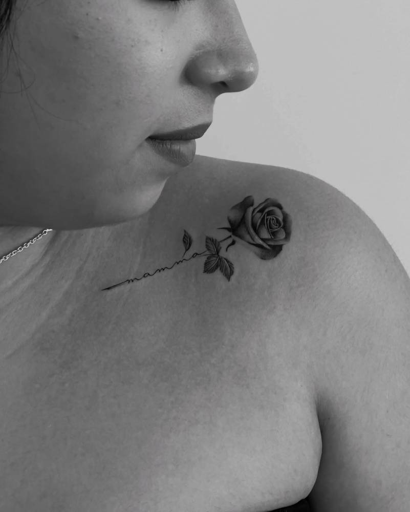 Black and grey rose and word "mamma" tattooed on the collarbone.