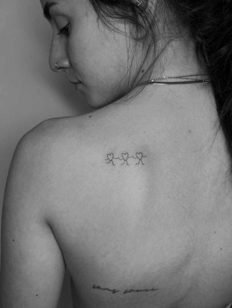 Minimalistic style hearts holding hands tattooed on the shoulder blade.