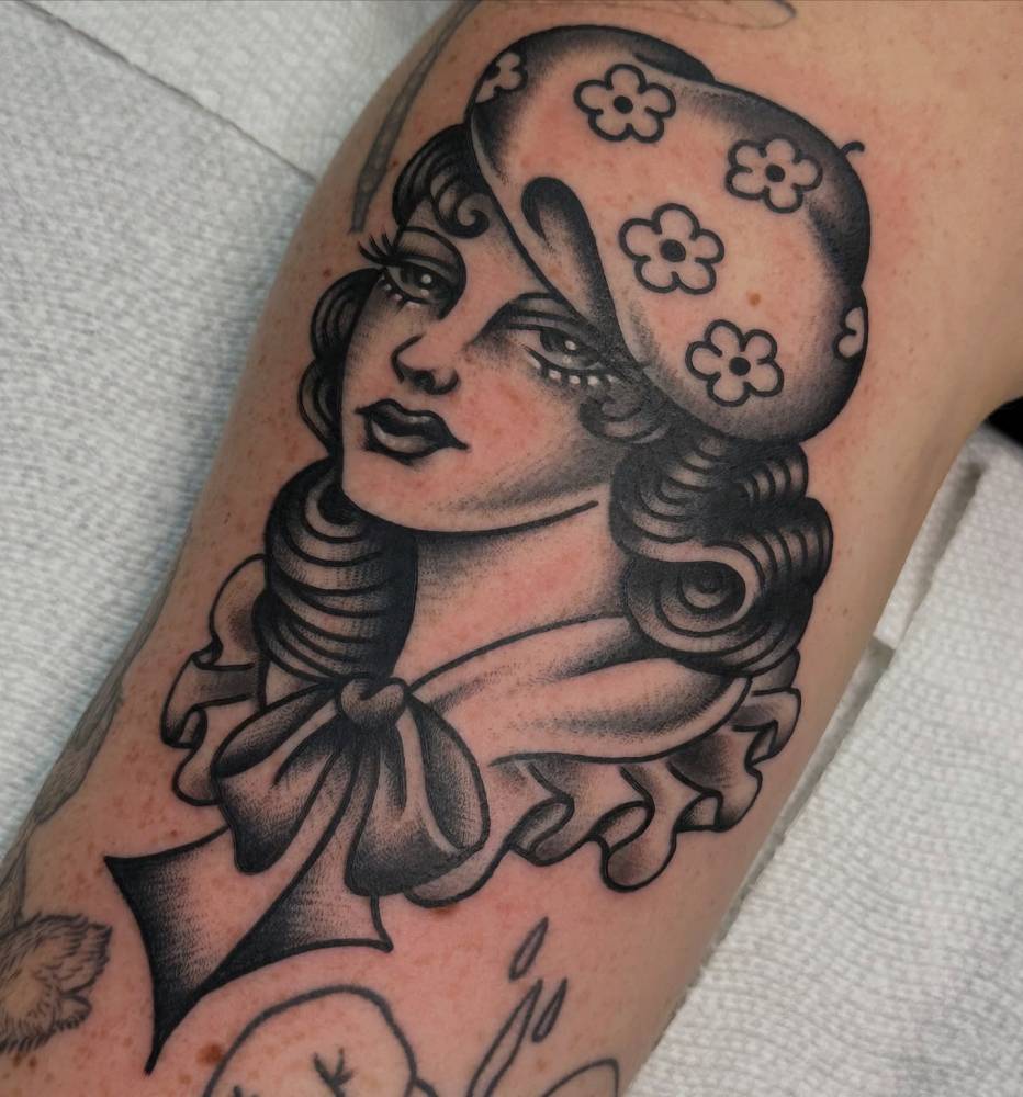 Woman portrait tattoo in traditional style located on the upper arm.