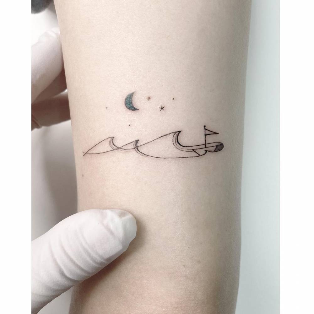 Wave, sailboat and moon tattoo located on the tricep, minimalistic style.