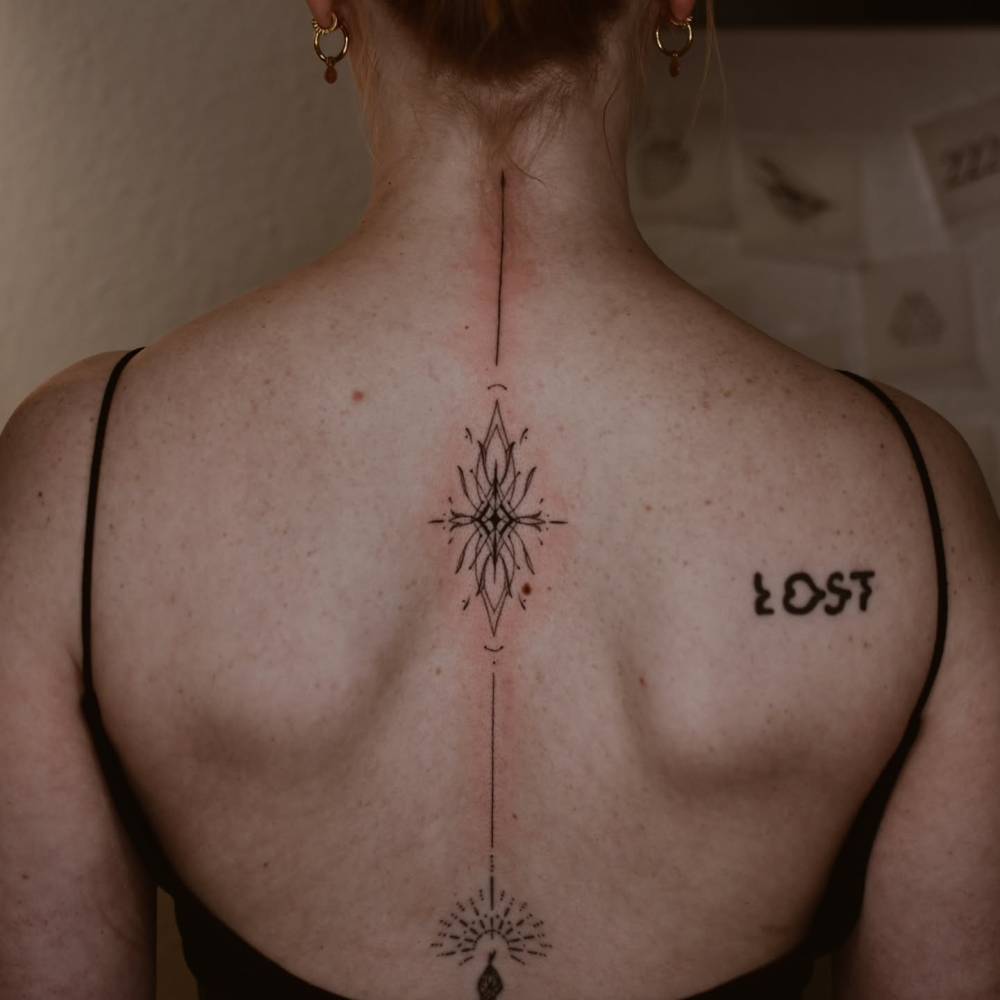 Line art style ornamental tattoo located on the spine.