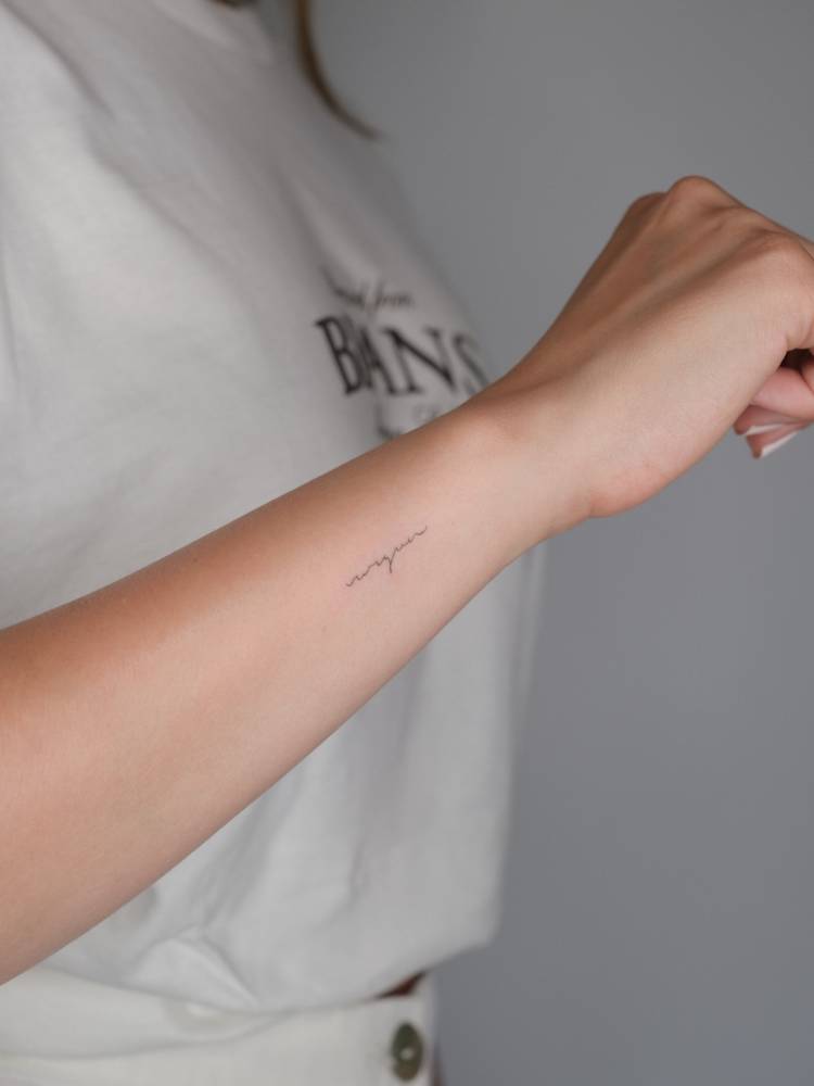 Handwritten font lettering tattoo located on the wrist.