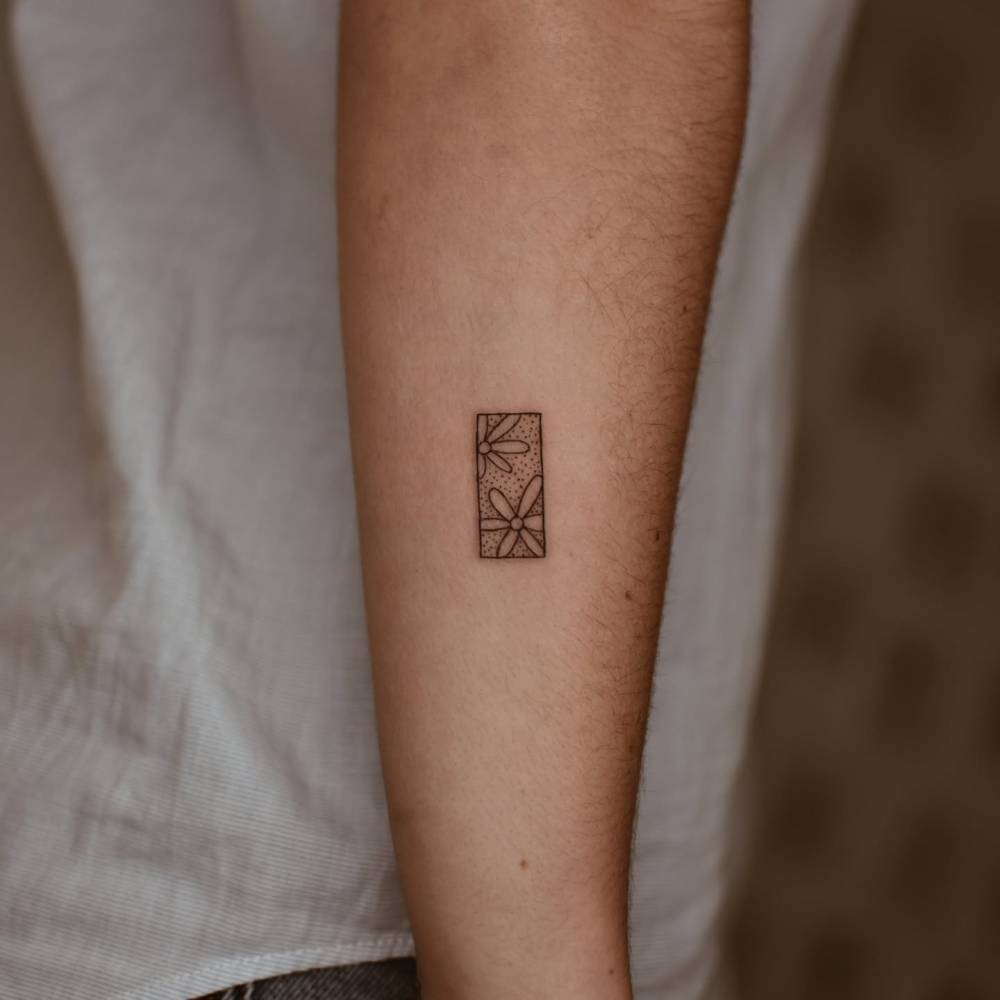 Flower tile tattoo in minimalistic style located on the forearm.
