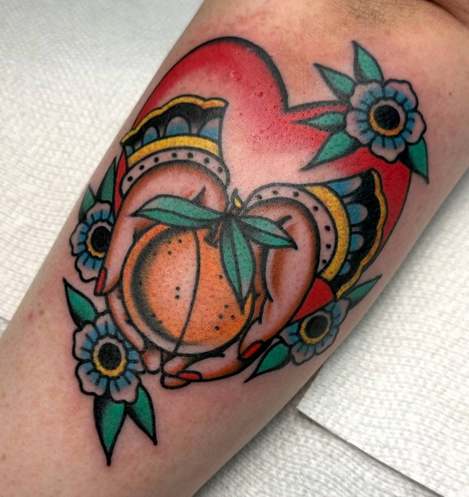 Hands holding an orange tattooed on the inner forearm, traditional style.