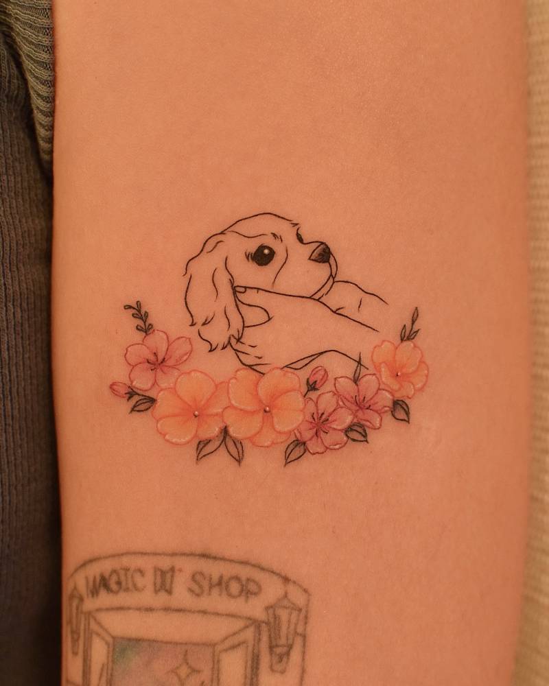Fine line style dog and flowers tattoo located on the upper arm.