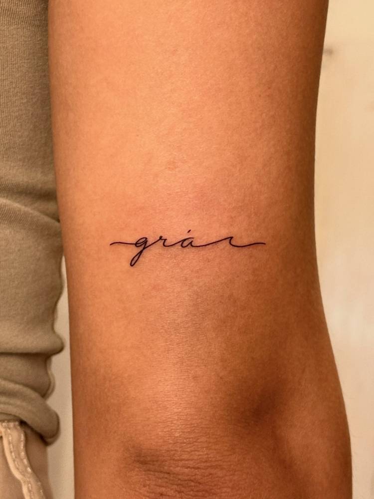 lettering tattoo of the word "grá" and wave placed on the tricep.