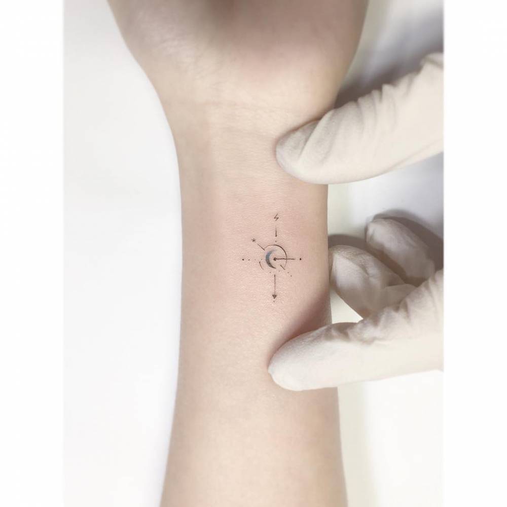 Compass rose tattoo located on the wrist, minimalistic style.