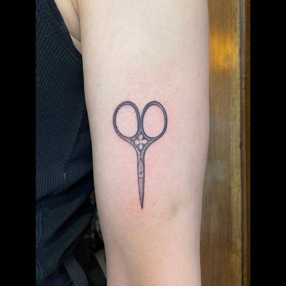 Illustrative style scissors tattoo located on the upper arm.