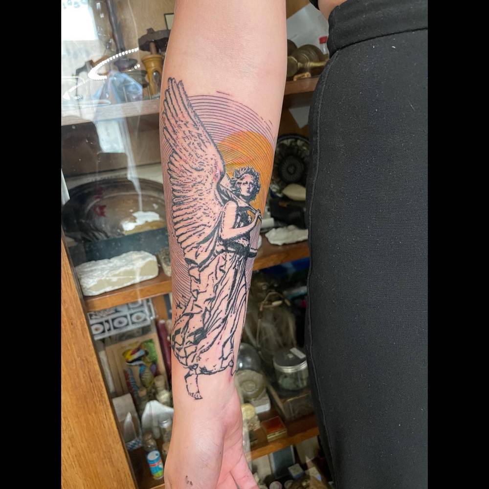 Graphic style angel tattoo located on the inner forearm.