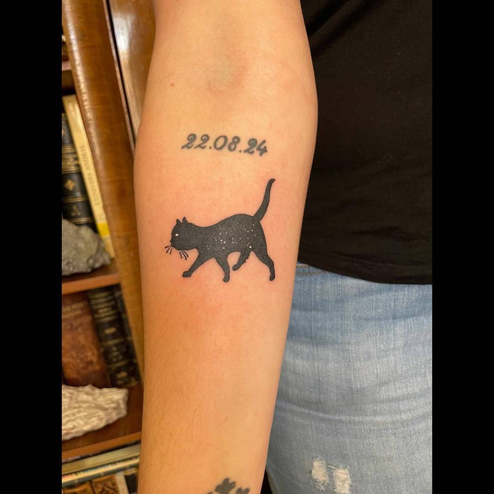 Black cat tattoo in illustrative style located on the inner forearm.