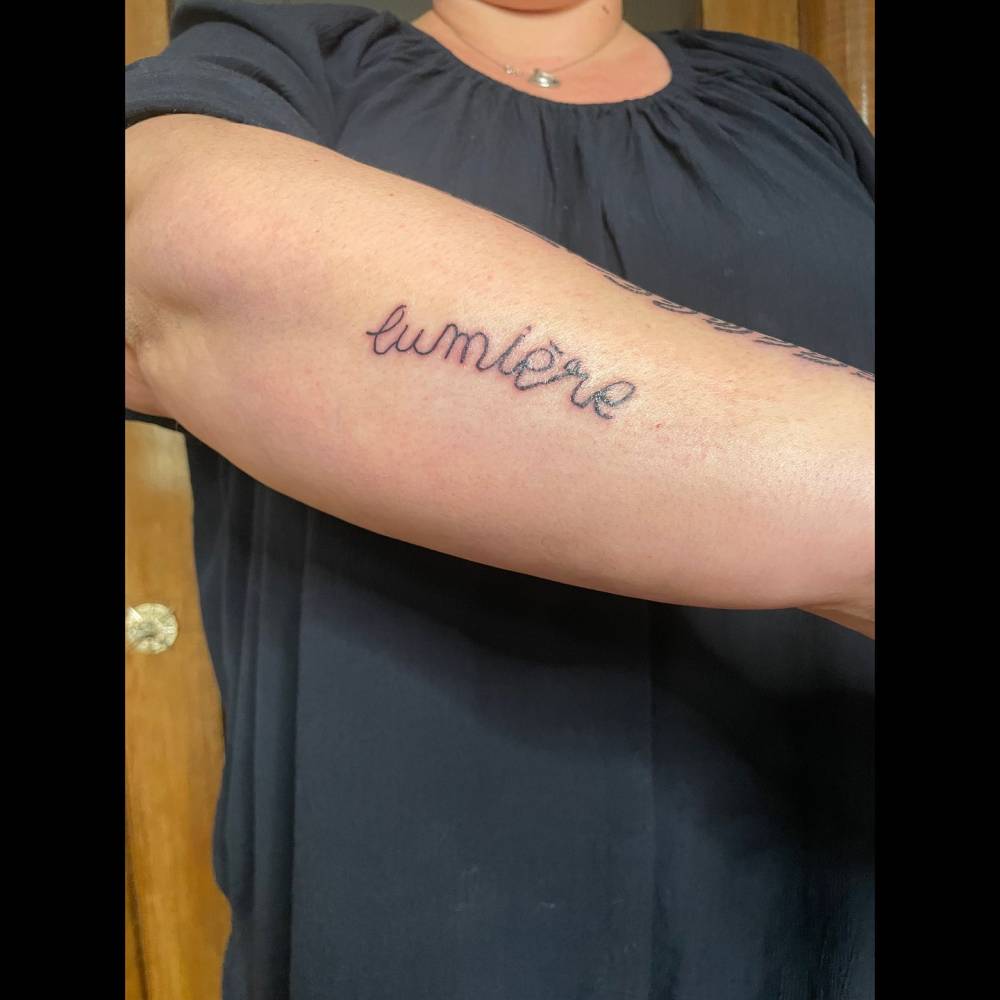 Lettering tattoo of the word "lumiére" written in her child's handwriting.
