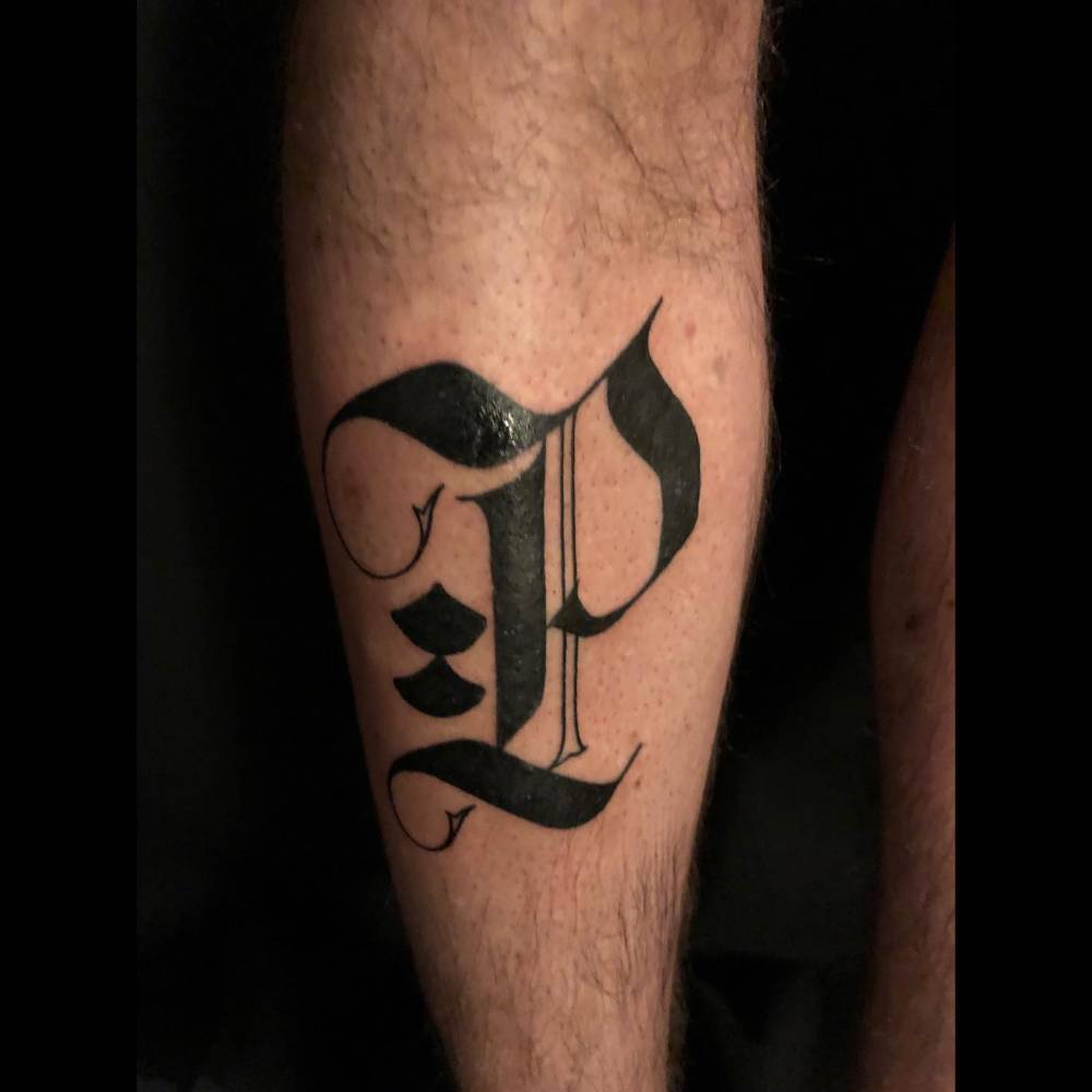 Gothic font letter "P" tattoo located on the shin.