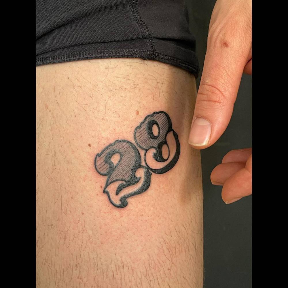 Lettering tattoo of the number "28" located on the thigh.