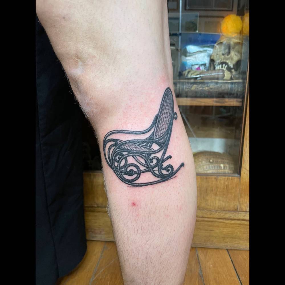 Illustrative style rocking chair tattoo located on the calf.