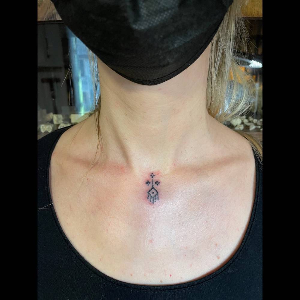 Tiny ornamental tattoo in blackwork style located on the collarbone.
