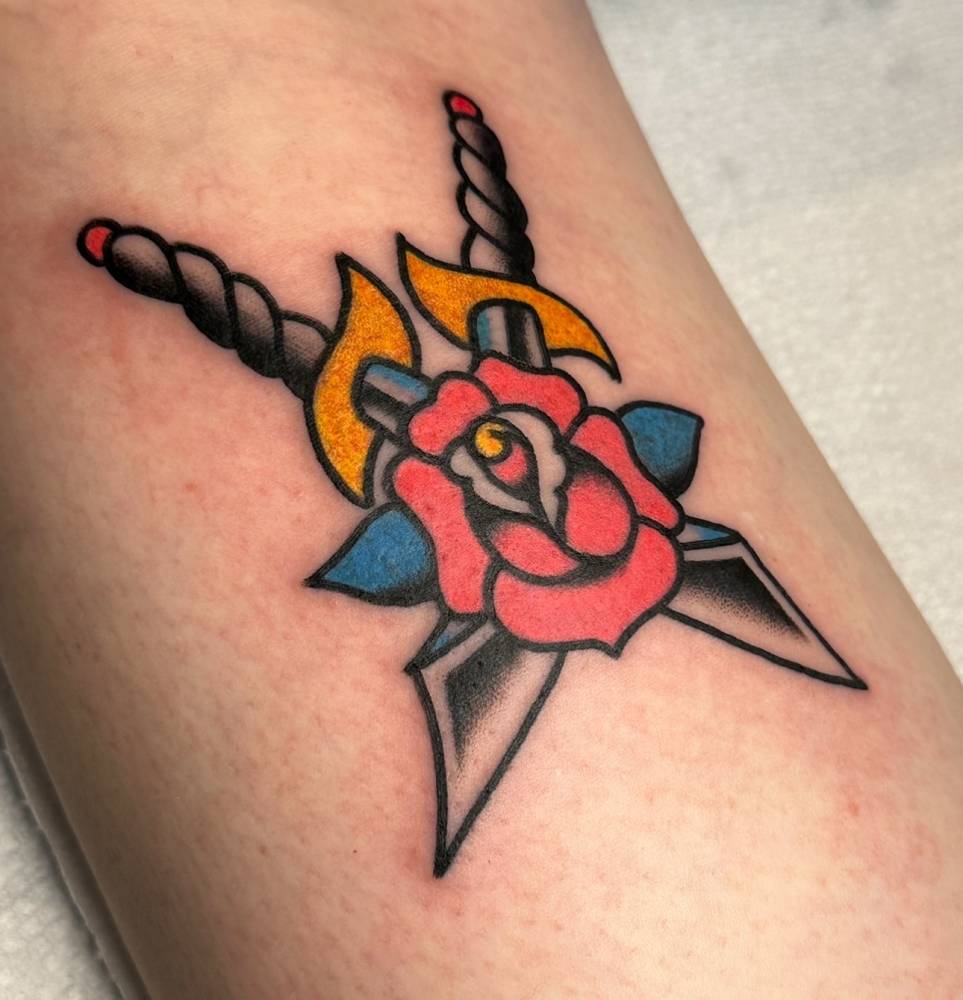 Scimitars and pink rose tattoo in traditional style placed on the inner forearm.