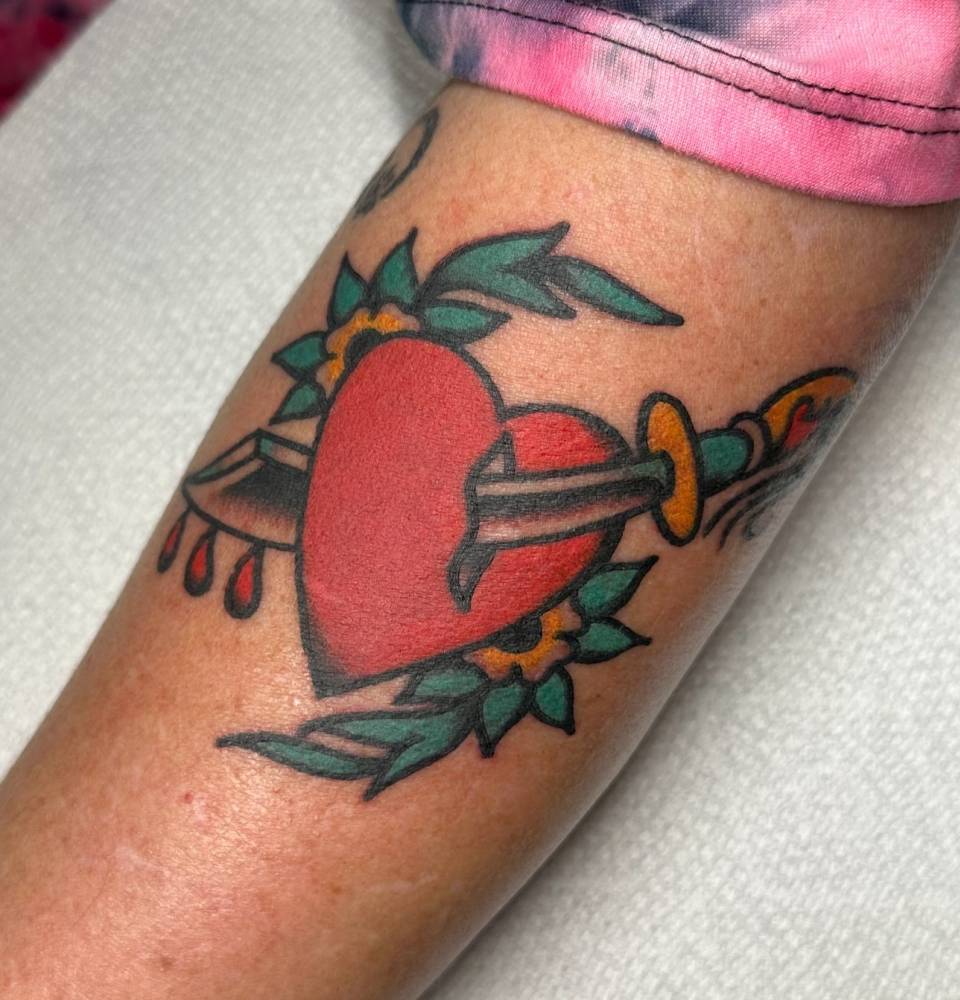 Heart and dagger tattoo in traditional style located on the upper arm.