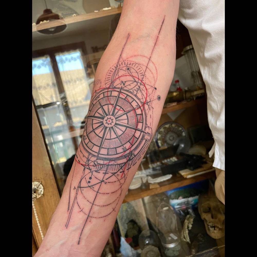 Compass rose tattoo located on the inner forearm, done in graphic style.