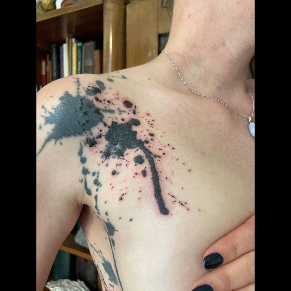 Ink splatter tattoo located on the shoulder, blackwork style.