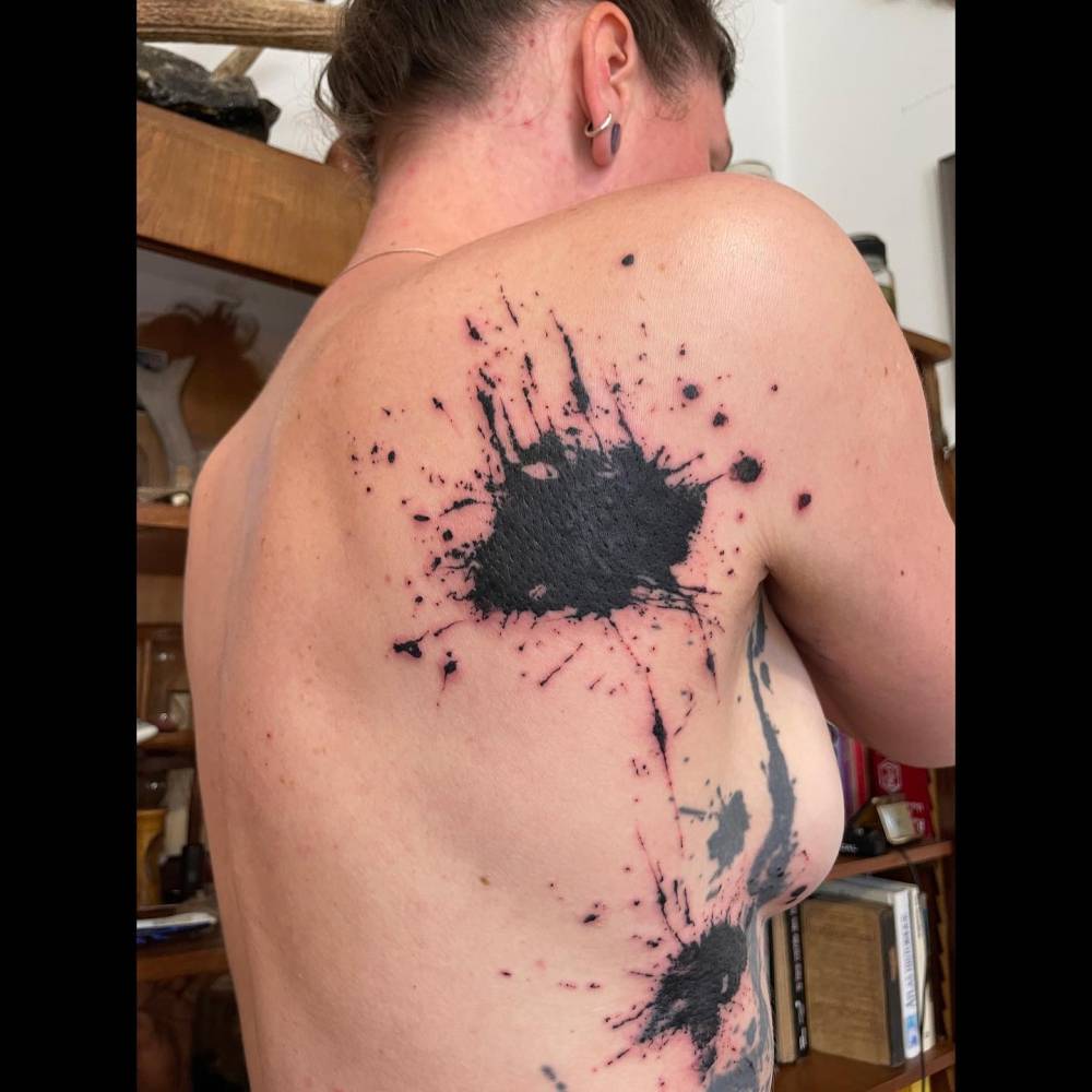 Watercolor style ink splatter tattoo located on the shoulder blade and rib.