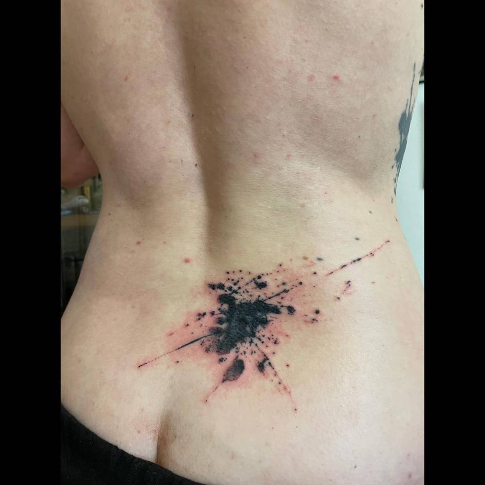 Watercolor style ink splatter tattoo located on the lower back.