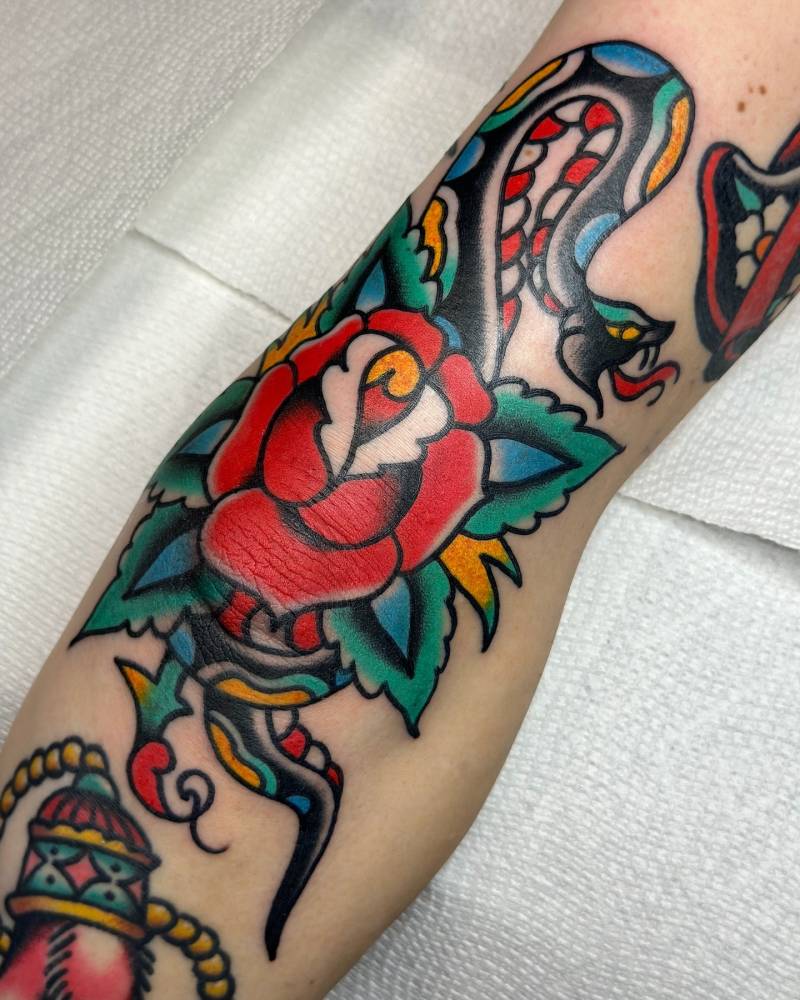 Red rose and snake tattoo located on the knee, traditional style.