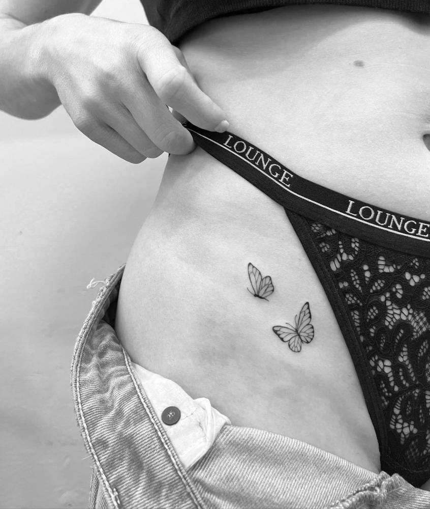 Fine line style butterfly couple tattoo located on the pelvis.