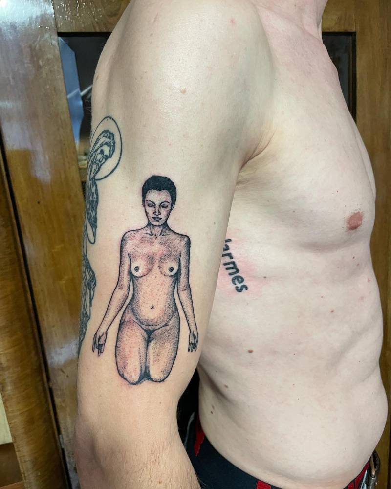 Nude woman tattoo in illustrative style located on the upper arm.