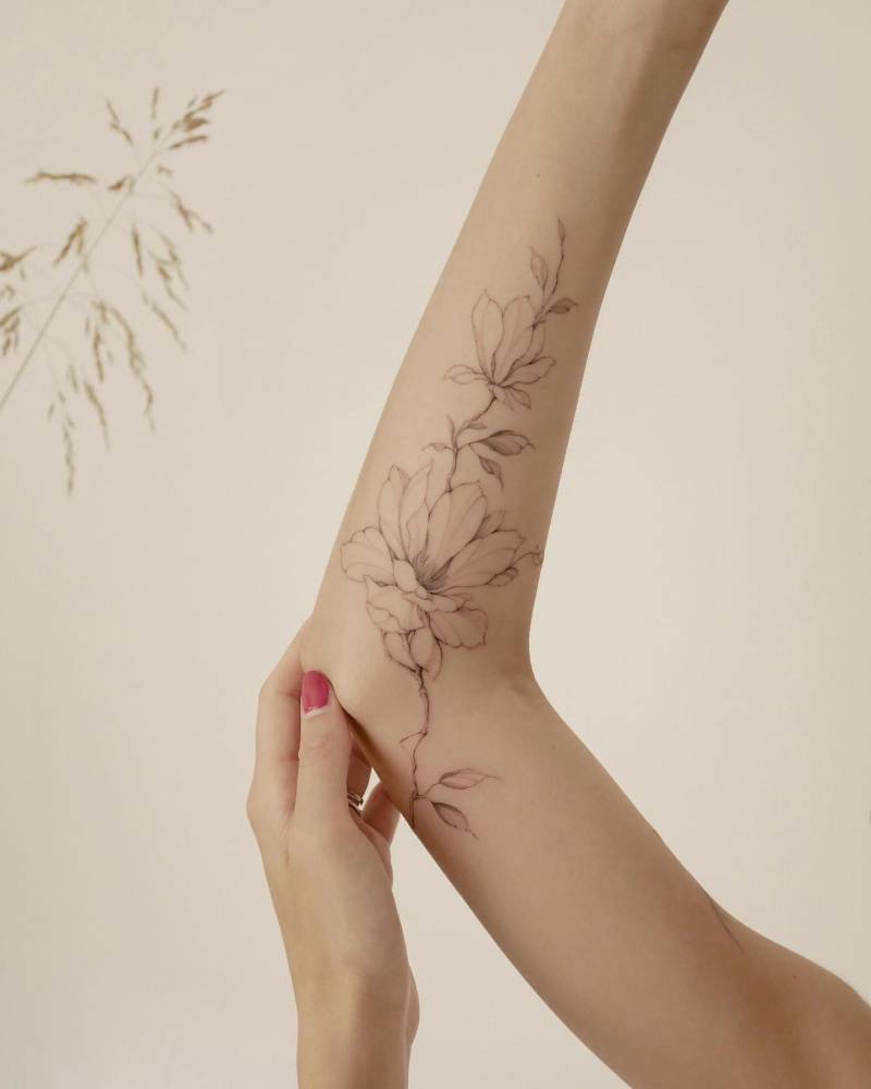 Freehand magnolia tattoo located on the arm, illustrative style.