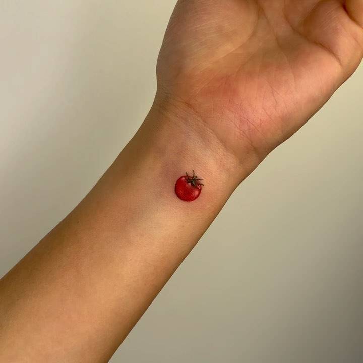 Micro-realistic style tiny tomato tattoo located on the wrist.