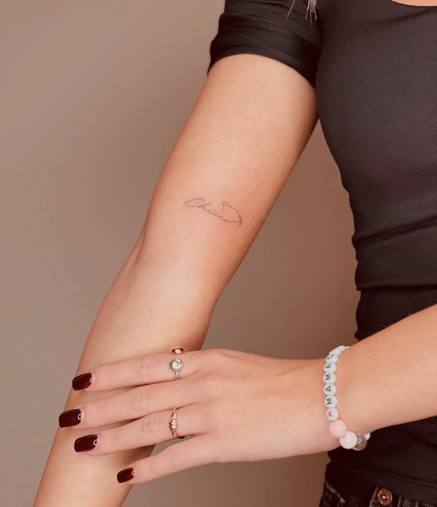 Fine line style dog ears and name "Chicco" tattooed on the inner arm.