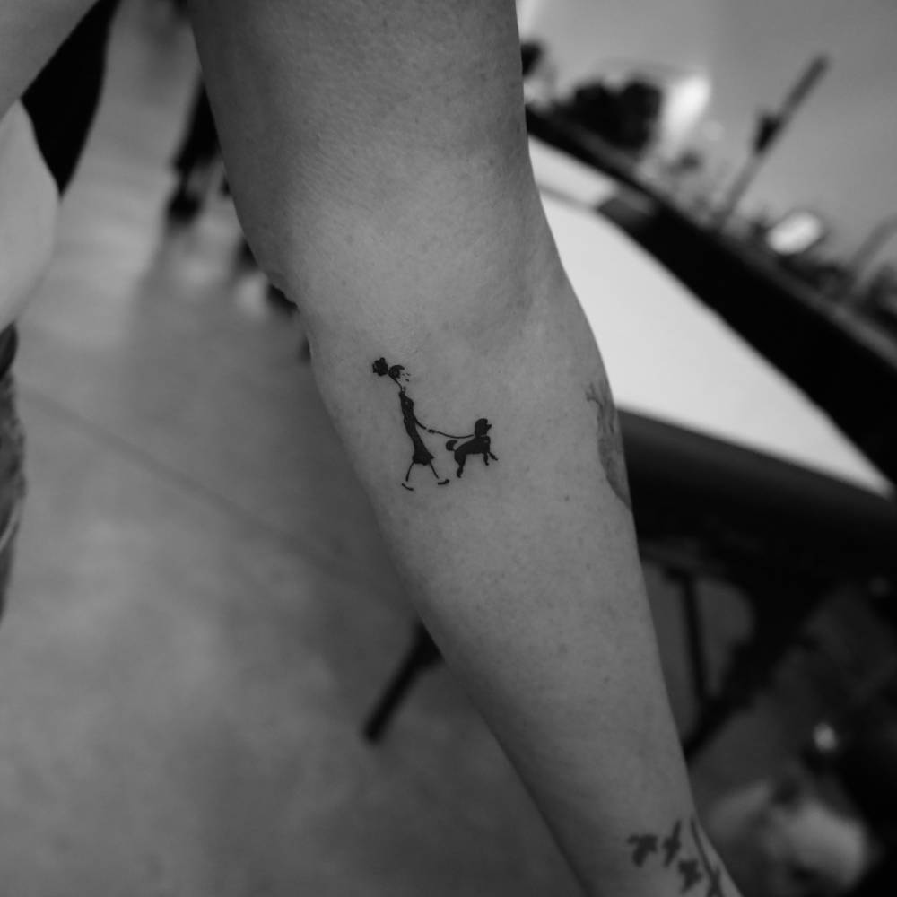 Woman walking a Poodle tattooed on the inner forearm.