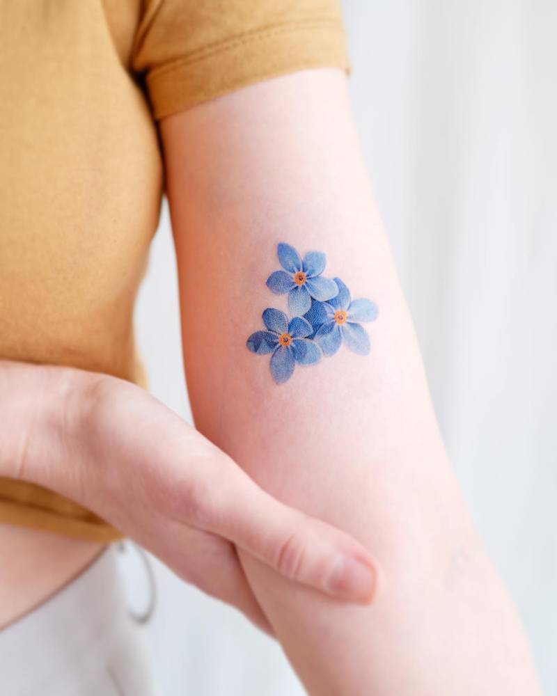 Watercolor style forget-me-not flowers tattoo located on the inner arm.