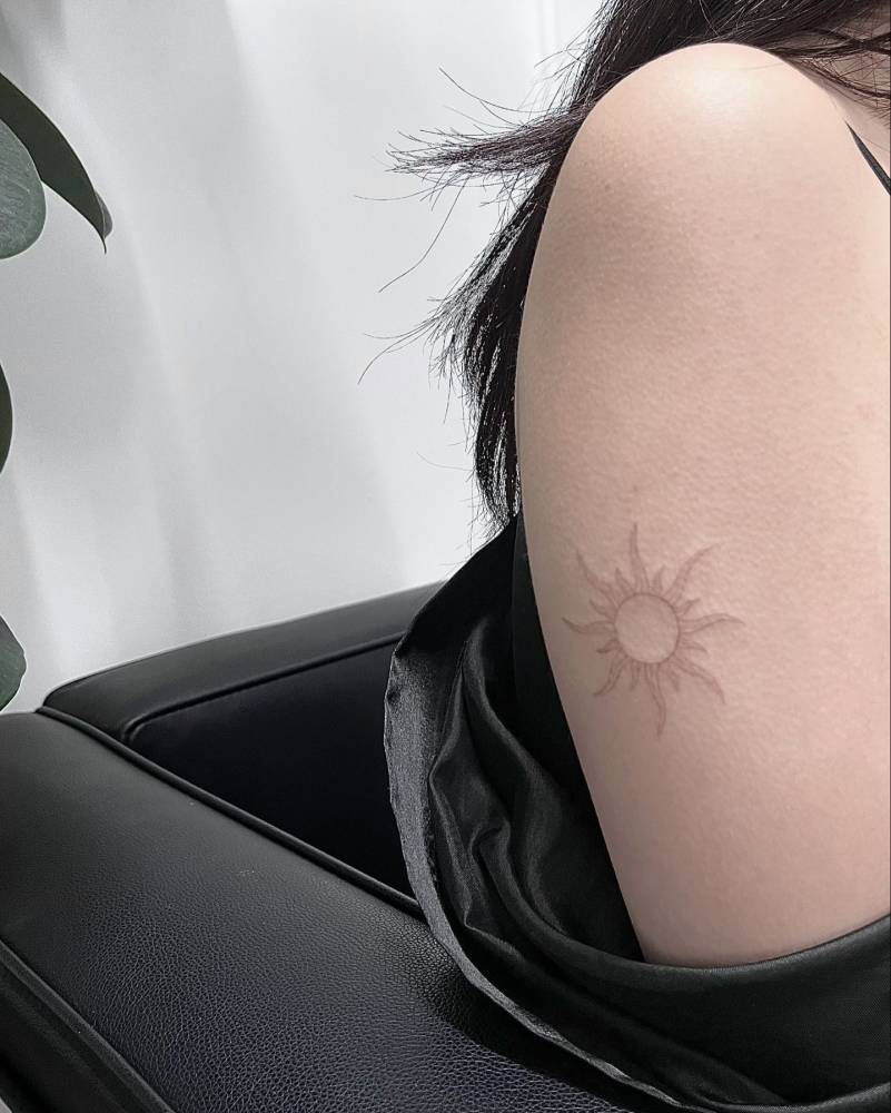 Sun tattoo in fine line style located on the upper arm.