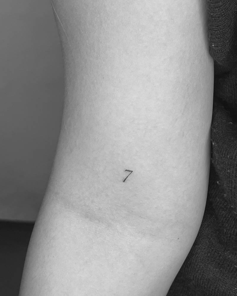Tiny lettering tattoo of the number "7" located on the inner arm.