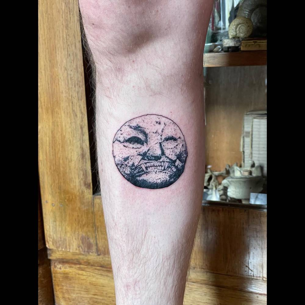 Moon face tattoo in blackwork style located on the shin.