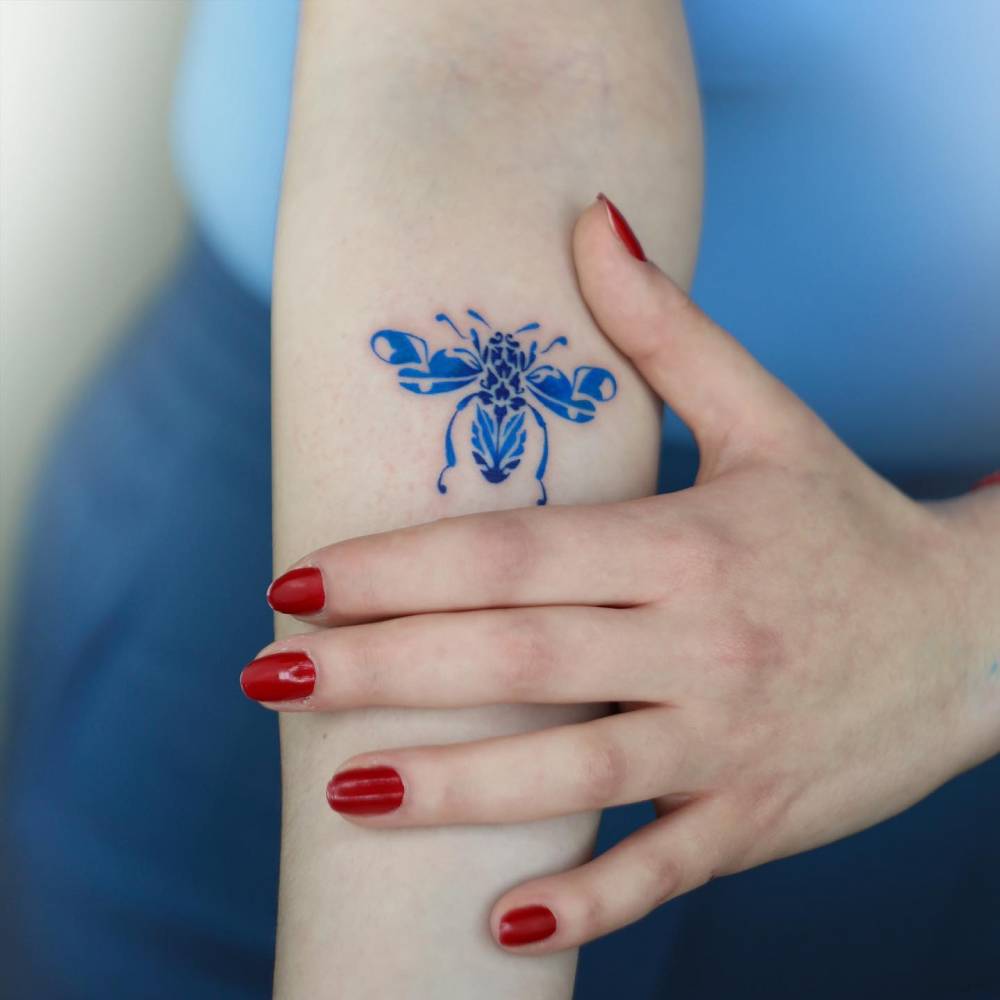 Illustrative style porcelain bee tattooed on the inner forearm.