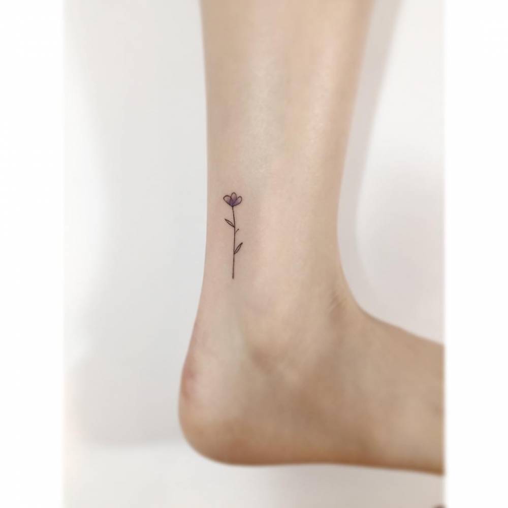 Little flower tattoo in minimalistic style located on the ankle.