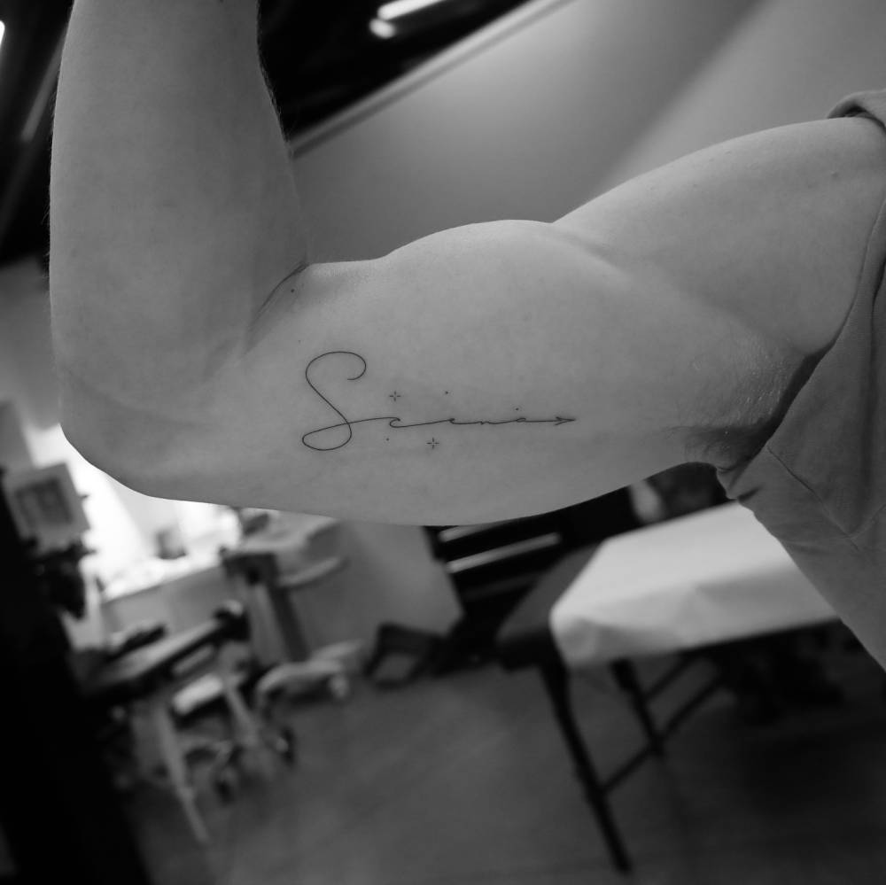 Handwritten lettering tattoo of the word "scena" located on the inner arm.