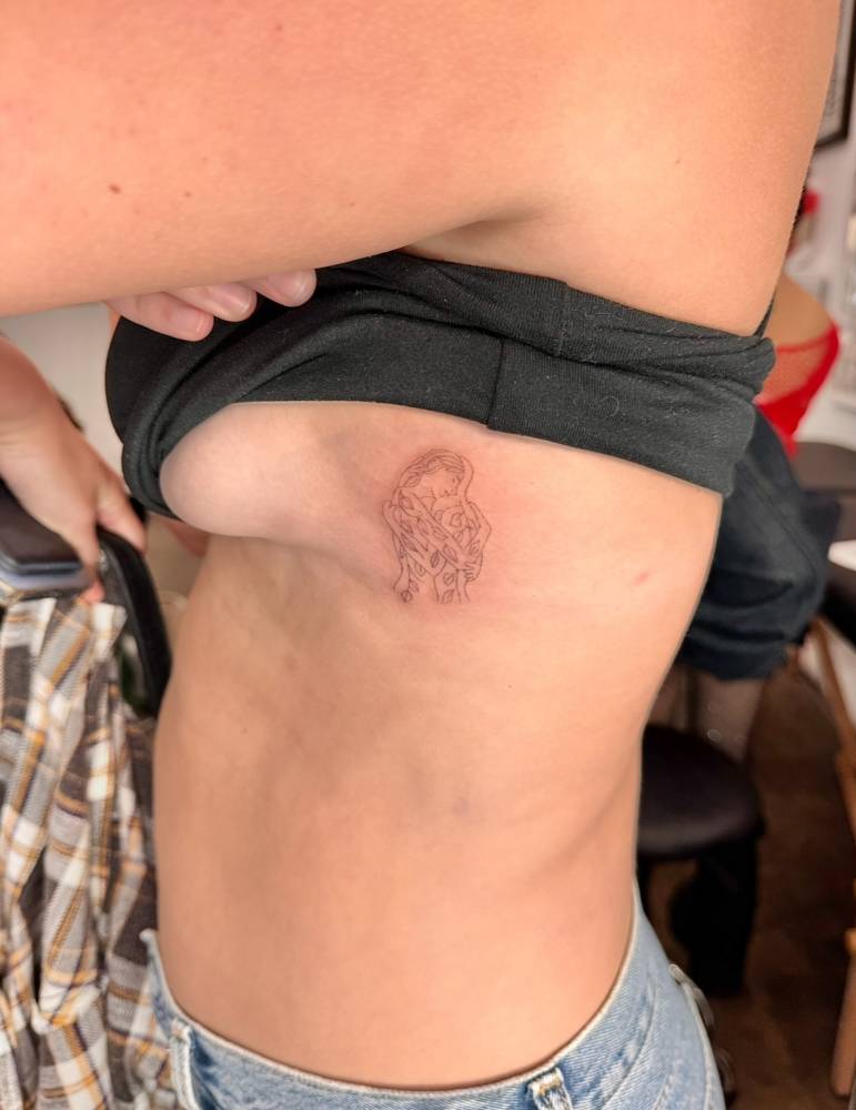 Fine line style hug tattoo located on the side boob.