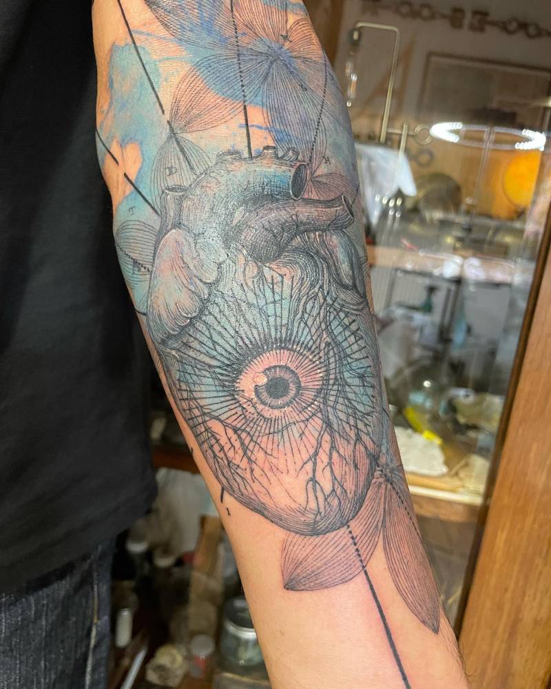 Graphic style anatomical heart and eye tattoo located on the inner forearm.
