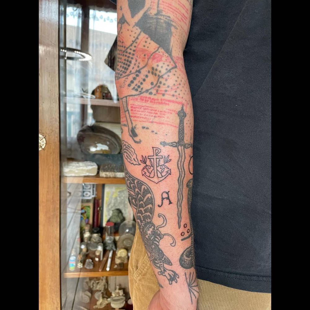 Anchor and letter "A" gap filler tattoos located on the forearm.