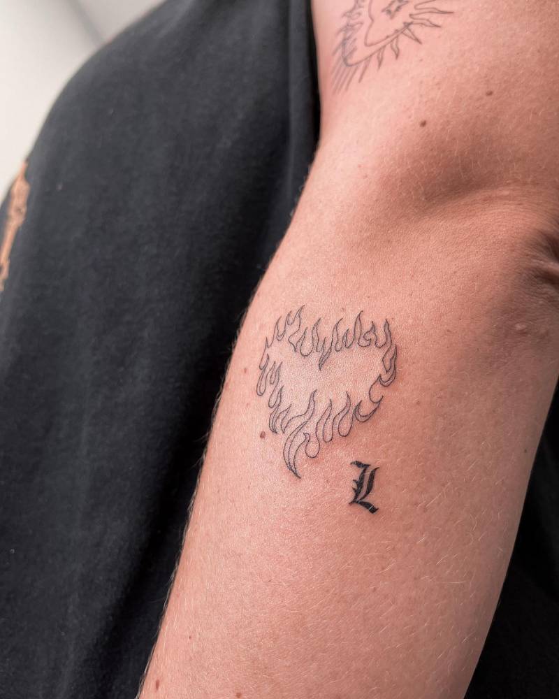 Flaming heart and letter "L" tattoo located on the forearm.
