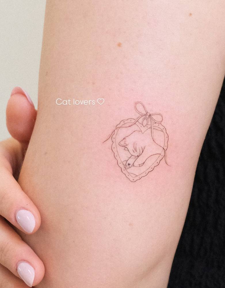 Cat pendant tattoo in fine line style placed on the tricep.