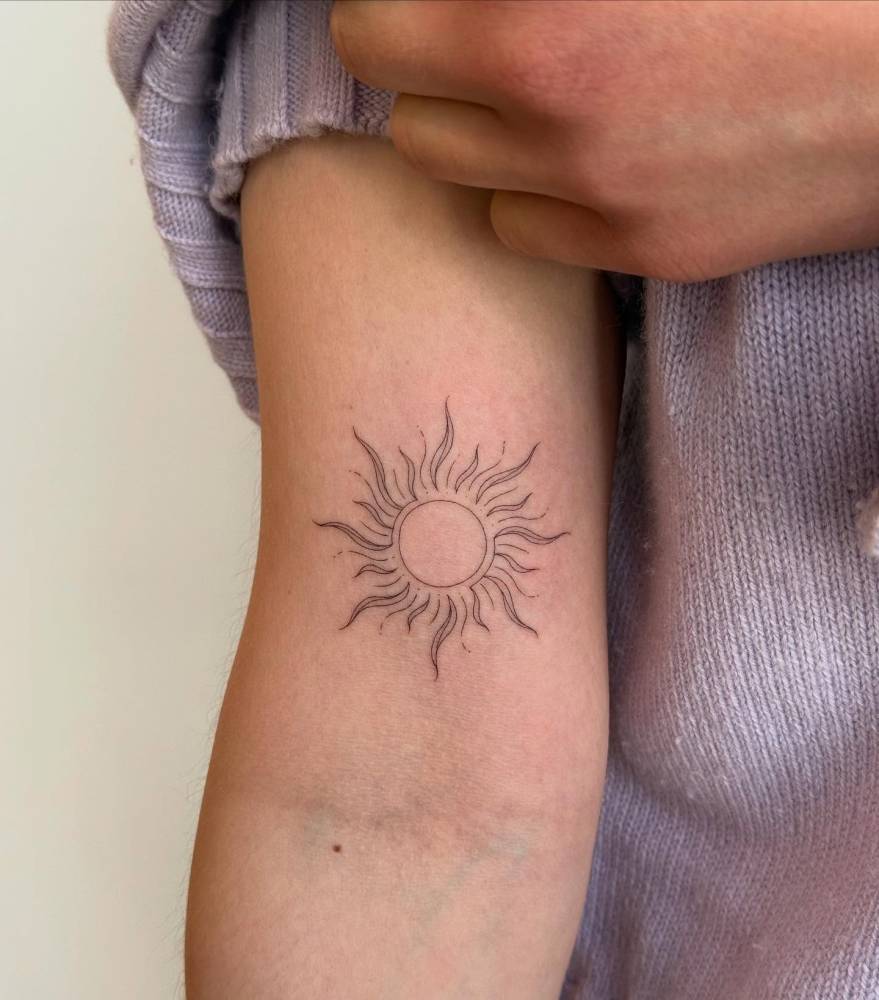 Fine line style sun tattoo located on the bicep.
