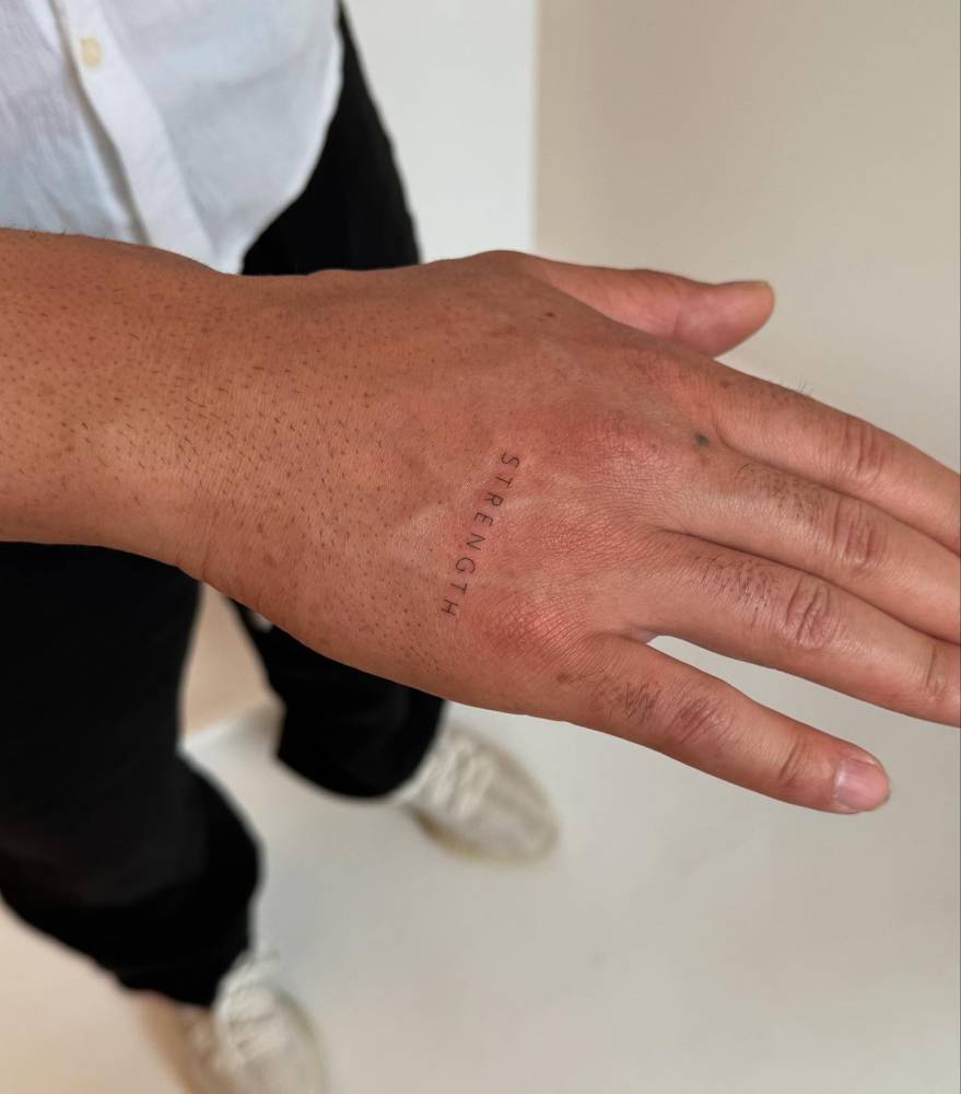 Lettering tattoo of the word "strength" located on the hand.