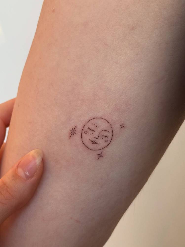 Little moon face tattoo in minimalistic style placed on the inner forearm.