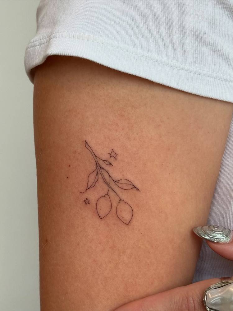 Lemon branch tattoo in fine line style located on the upper arm.