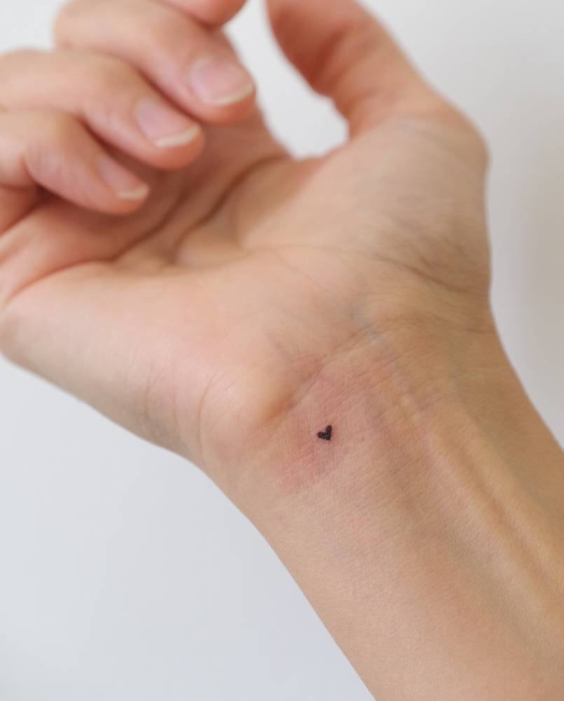 Micro heart tattoo located on the wrist, done in minimalistic style.