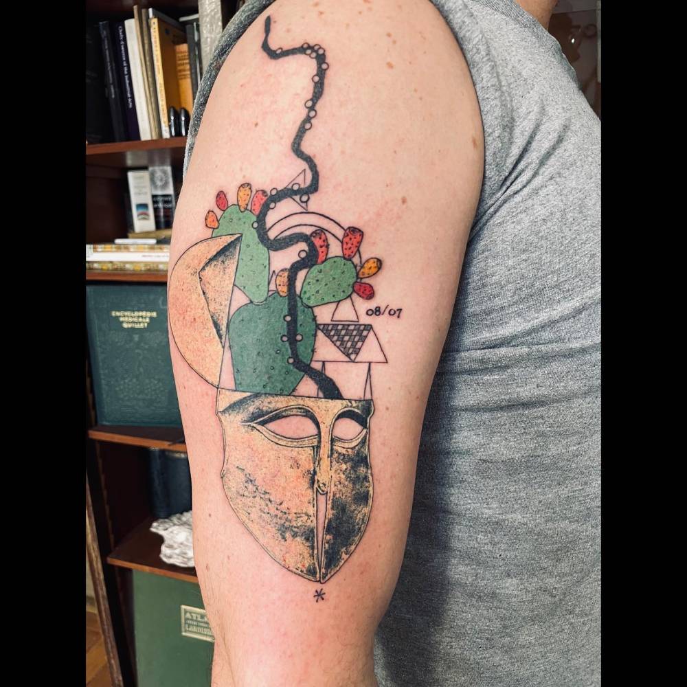 Graphic style cactus and mask tattoo located on the upper arm.